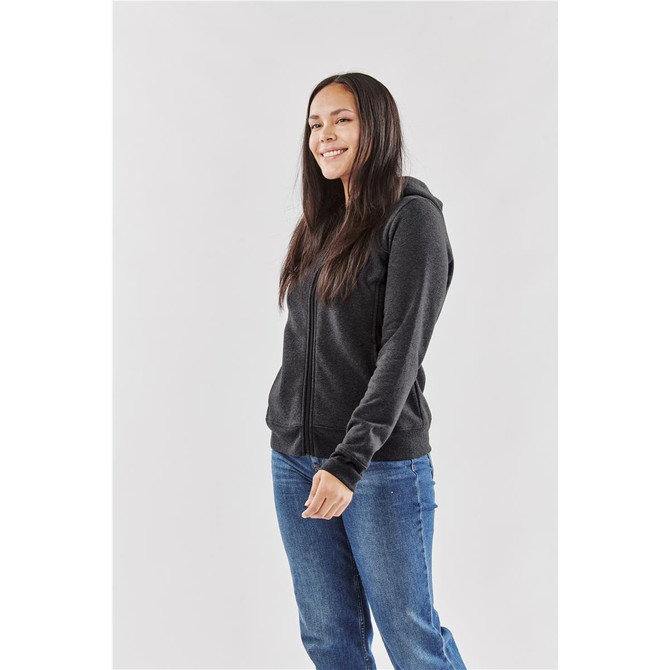 A woman wearing a black fleece full zip hoodie, styled with a neutral background and casual blue jeans.