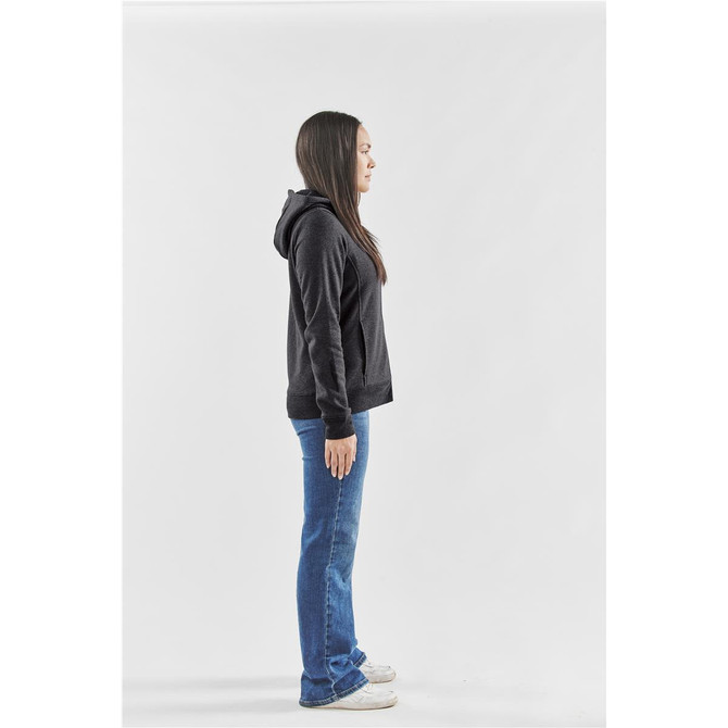 A woman stands sideways wearing a black fleece full zip hoodie paired with blue jeans and white sneakers.