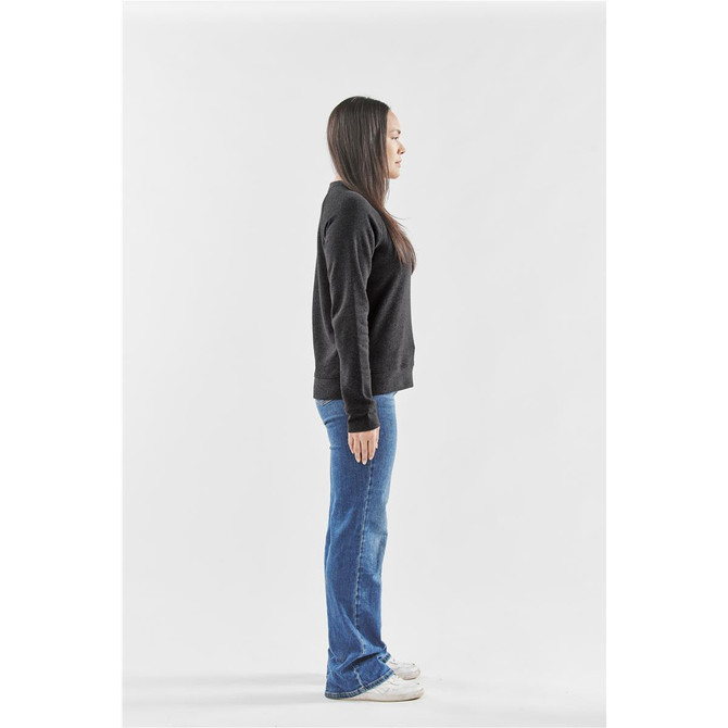 A woman stands sideways wearing a black fleece crew neck jumper and blue jeans, with white sneakers.