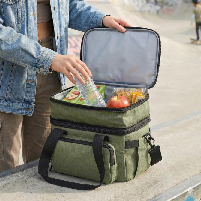 A green expanding cooler being filled with a water bottle, snacks, and an apple, resting on a ledge.