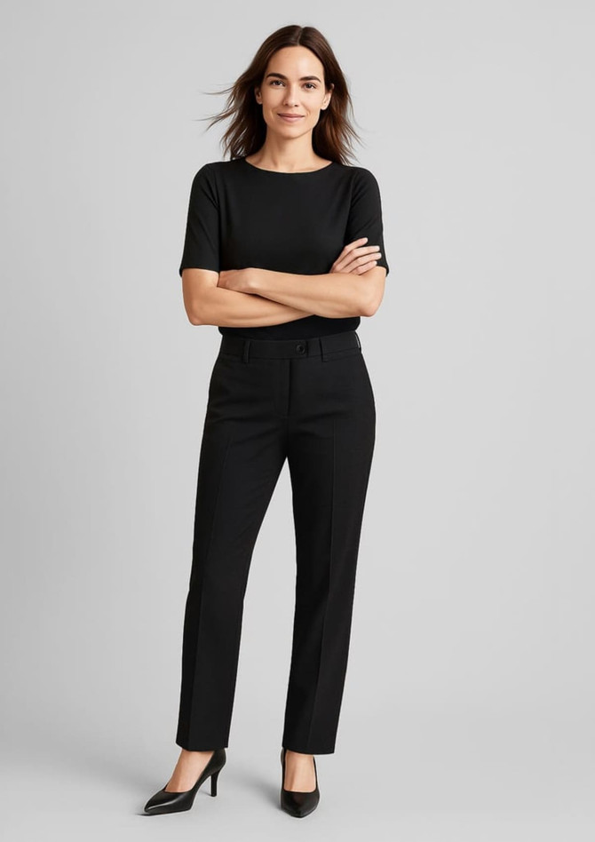 A woman wears black comfort wool stretch relaxed pants paired with a black top and high heels, standing confidently.