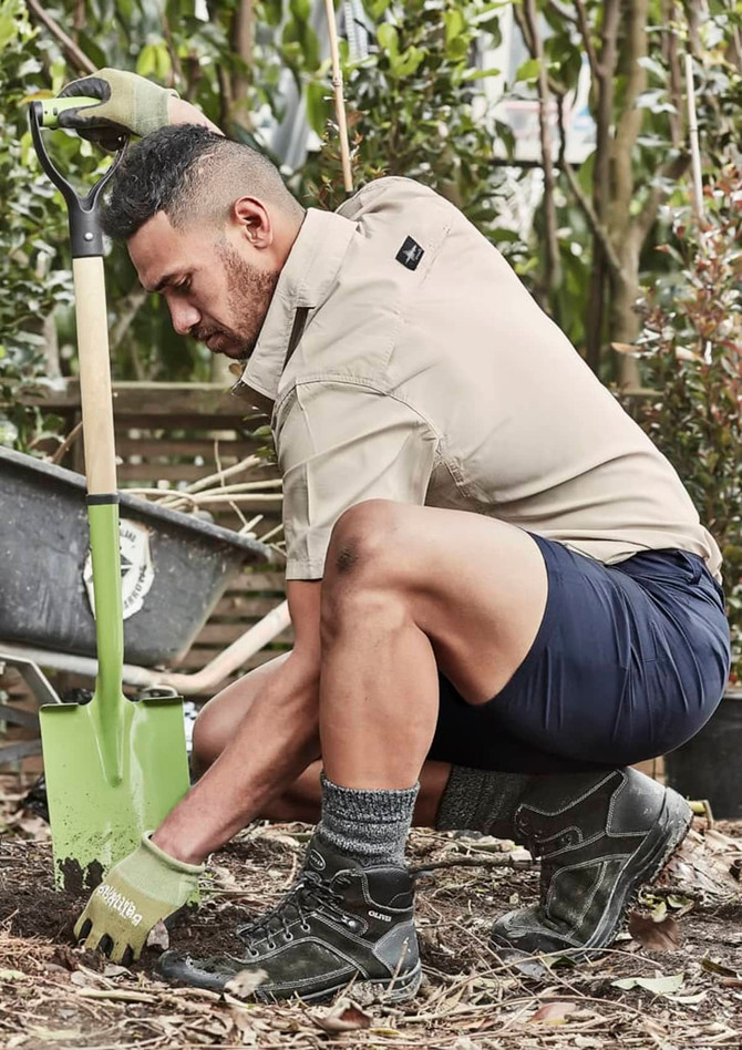 Men's lightweight outdoor shorts in navy, paired with a beige shirt, worn by a man kneeling with a shovel in a garden.