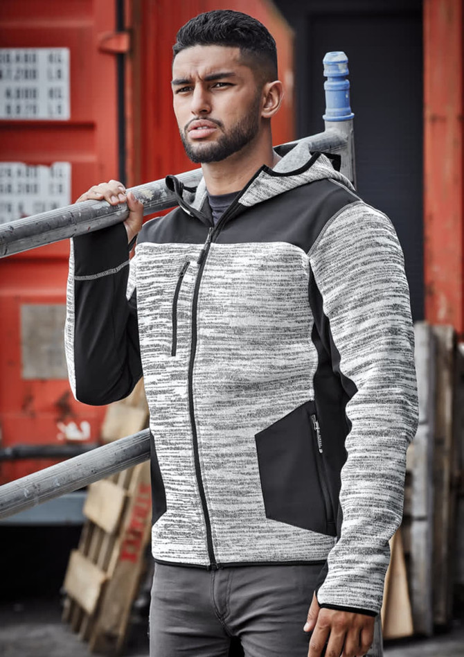 A man wearing a black and grey striped unisex reinforced knit hoodie, holding a metal ladder against a red backdrop.