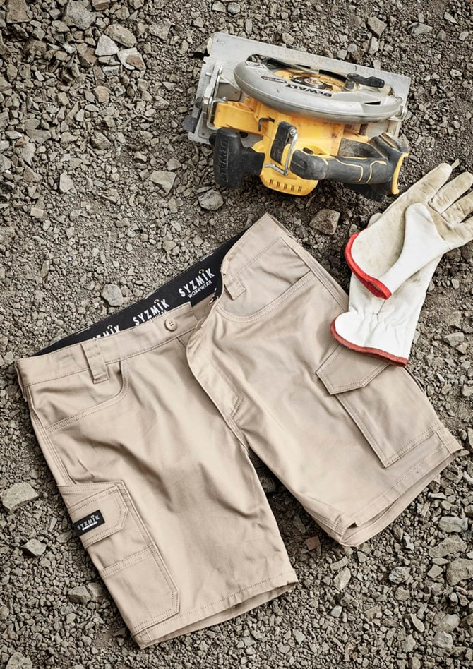 Mens Essential Stretch Cargo Shorts in beige, laid out on gravel, alongside a power tool and gloves. Features branding.