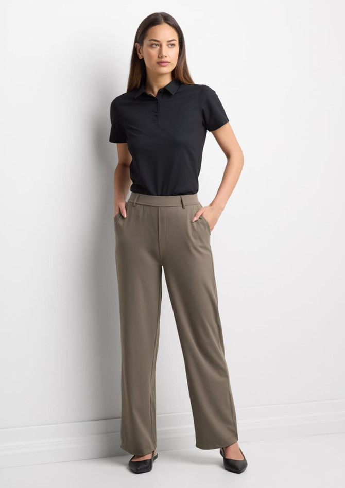 A woman wearing a black short sleeve polo shirt paired with beige trousers, standing confidently with her hands in her pockets.