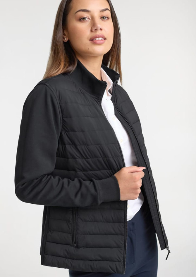 A women's tailor jacket in black, featuring a quilted design and a zip closure. A model is wearing it with a white shirt.