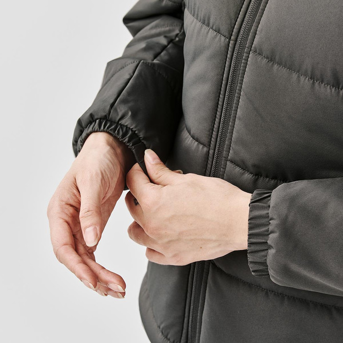 A close-up of a woman's hands adjusting the cuff of a women's grey puffer jacket. The jacket has a logo.