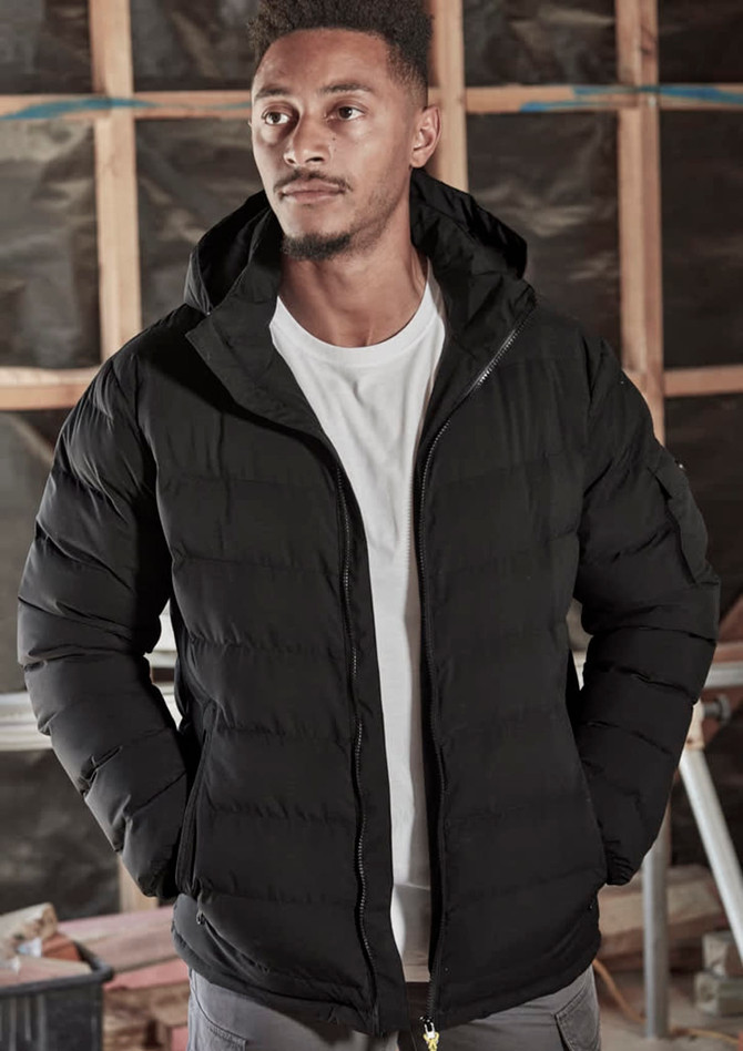 A black unisex hooded puffer jacket with a zip front, worn by a model in a construction setting.