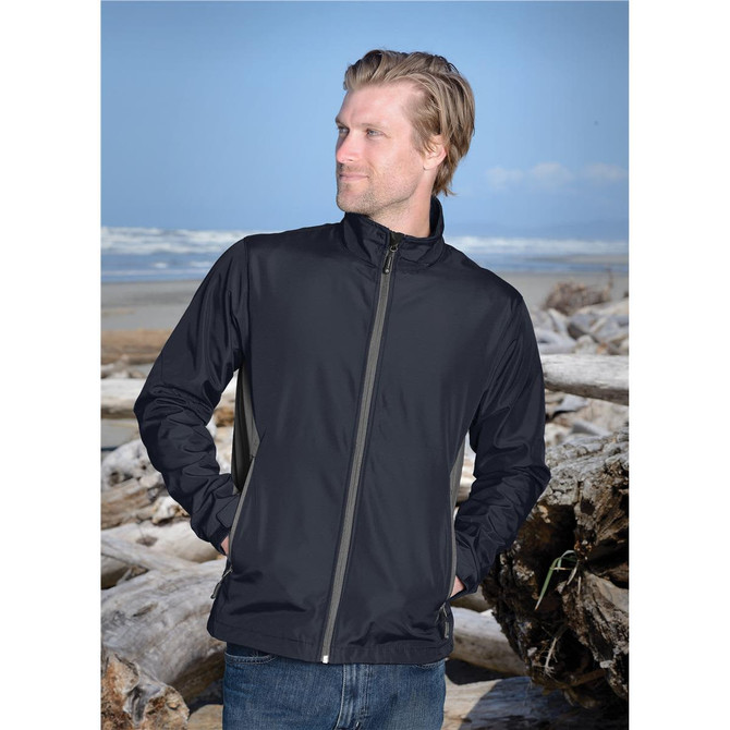 A black men's softshell jacket is displayed against a beach backdrop with driftwood. The jacket features a zip front and has a logo.