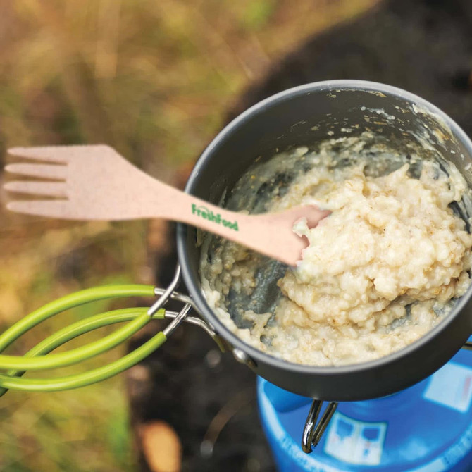 A cooking pot containing a creamy mixture with a green handle and a wooden fork labeled "freshfood" resting inside it.