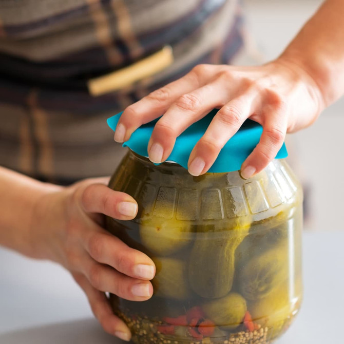 A drink bottle with a blue silicone lid being opened, revealed to contain pickles inside a glass jar.