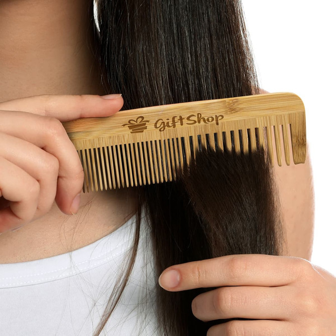A bamboo hair comb featuring a logo, held in a person’s hand, with straight hair being combed.