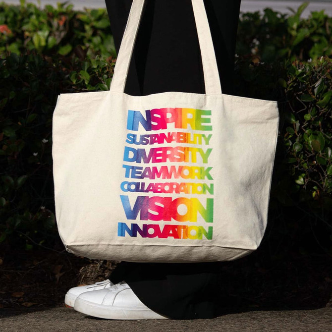 A zippered cotton canvas shopper tote in natural colour with a rainbow of text highlighting various positive themes.