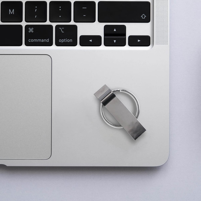 A silver Titan Flash Drive placed on a laptop's keyboard, alongside a minimalistic desk setup.