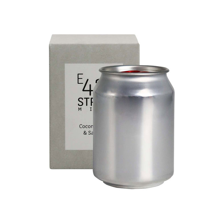 A silver can candle sits beside a square grey box, showcasing a sleek design and minimal branding.