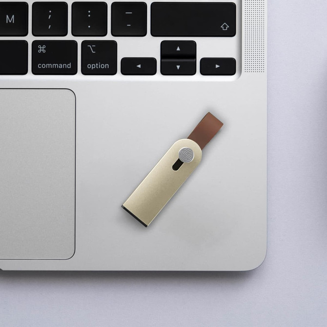 A sliding metal flash drive in gold and brown is placed on a laptop keyboard. The drive has a logo.