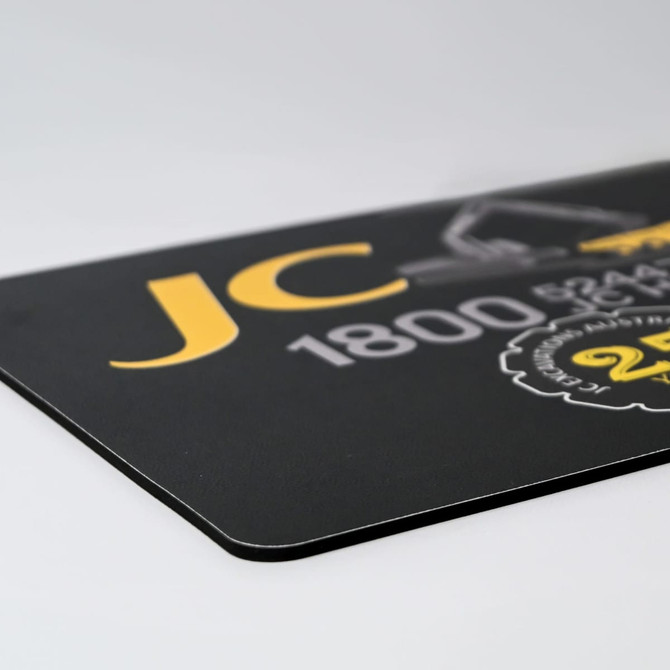 A fabric mouse mat in black with yellow accents and a logo. The dimensions are 225mm x 185mm.