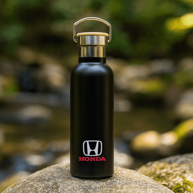 A drink bottle in matte black with a metal lid and a logo on the front, set against a natural background.