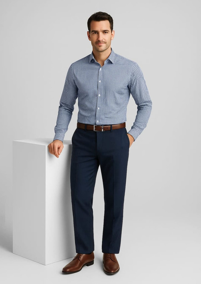 A man wearing a blue checked shirt and navy flat front pants, standing next to a white display. The pants have a branding logo.