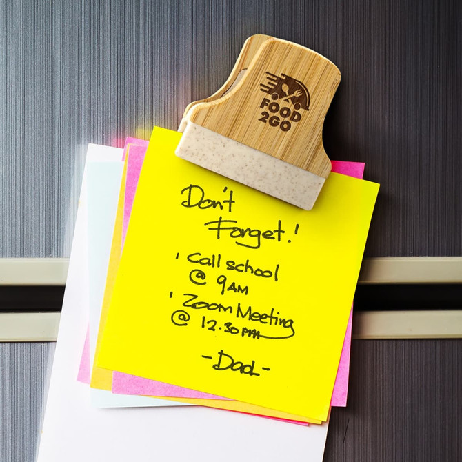 A bamboo clip holding several colourful sticky notes on a fridge, featuring a smooth finish and a logo.