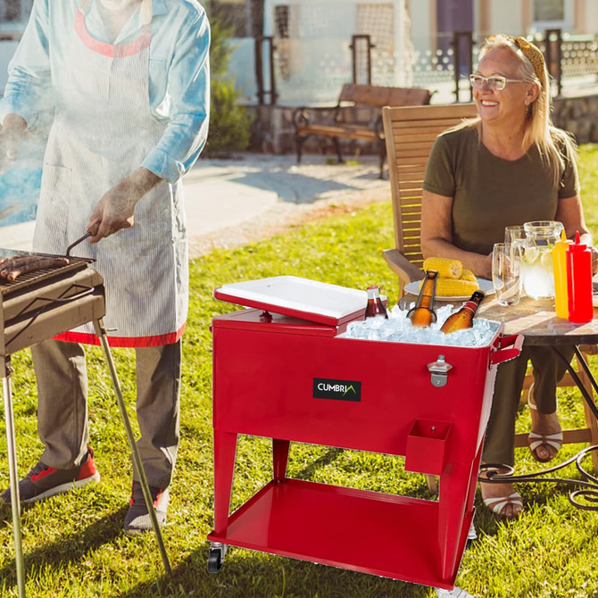 A red cooler box trolley filled with ice and drinks, positioned near a barbecue and a woman sitting outdoors.