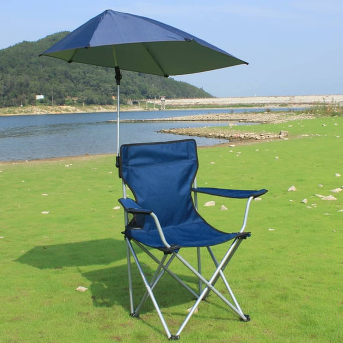 A navy blue adjustable umbrella attached to a folding camping chair by a universal clamp, set by a lake.