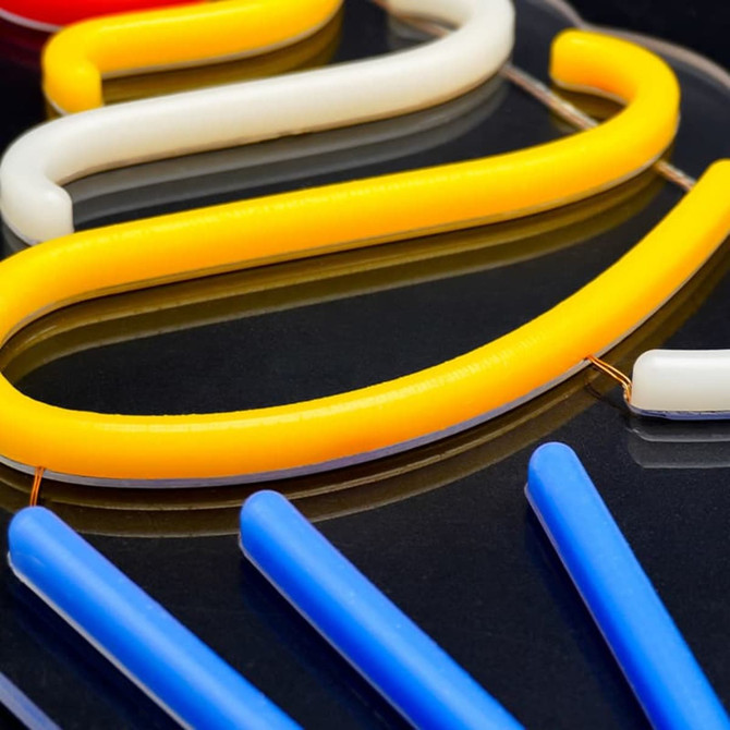A vibrant neon LED sign design featuring yellow, white, and blue flexible tubes against a black surface.