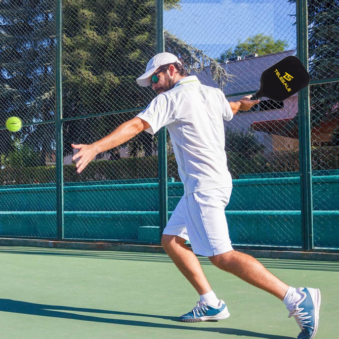 A player in a white outfit swings a black pickleball paddle on a green court, with a ball approaching.