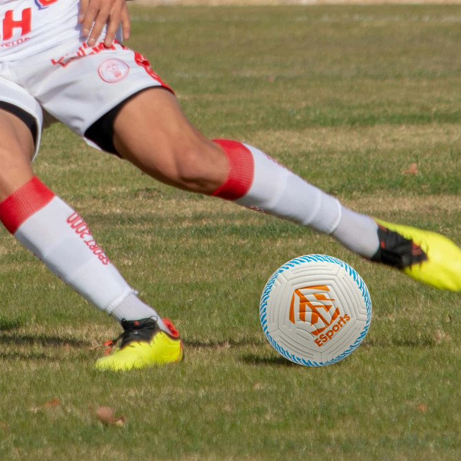 A premium white and blue soccer ball with a logo, positioned on a grassy field near a player in action.
