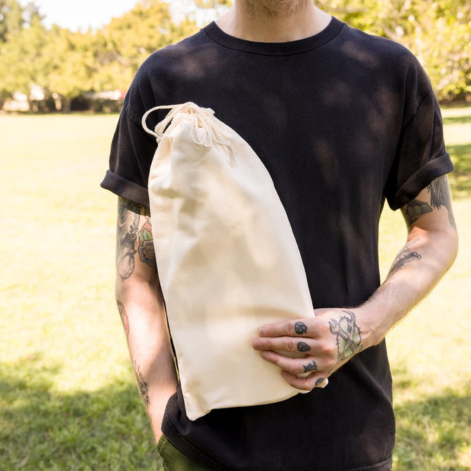A beige drawstring bag held by a person in a black shirt, set against a green outdoor background.