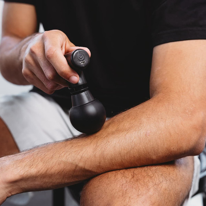 A black mini massage gun held by a person, focused on the arm, with a simple design and small size.