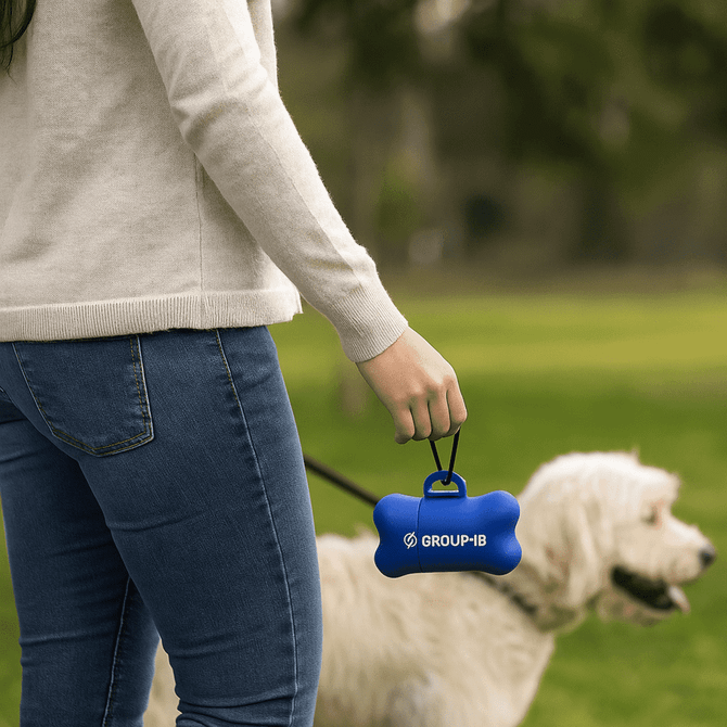 A blue dog waste bag dispenser shaped like a bone is held by a person walking a dog in a grassy park.