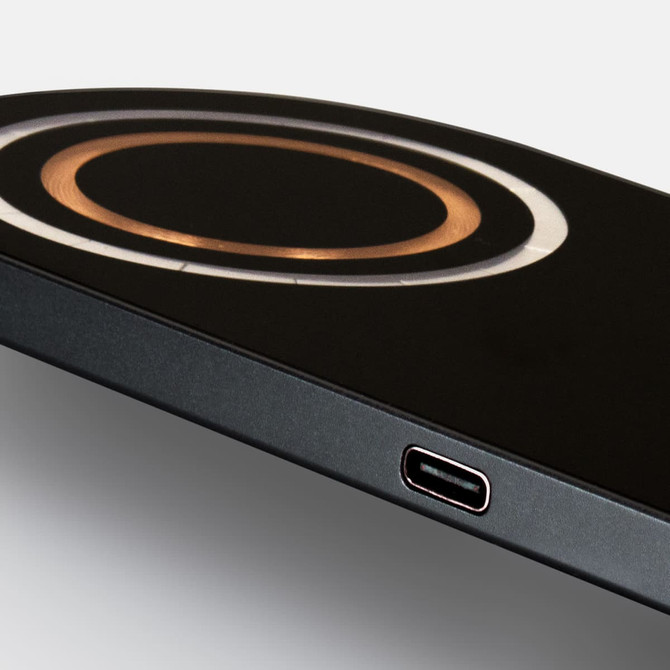 A sleek black wireless charger features a circular charging area in gold. Includes a USB-C port.