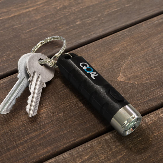 A rechargeable torch keyring in black and silver, attached to a set of keys on a wooden surface.