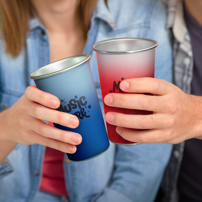 A drink cup in blue and a cup in red, both with a silver rim and featuring a logo, held by two people.