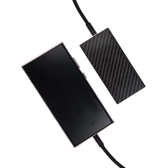 A smartphone connected to a charging cable with a sleek, carbon fiber design power bank.