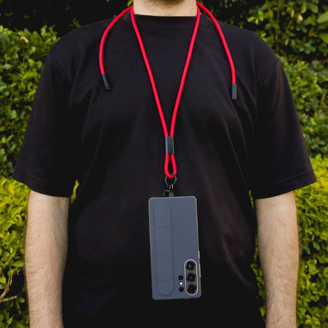 A phone lanyard in red with a grey phone attached, worn around the neck against a green background.