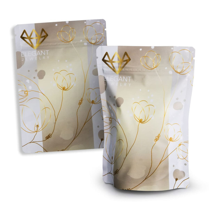 A small foil stand-up pouch in white and gold with a floral design and a logo.