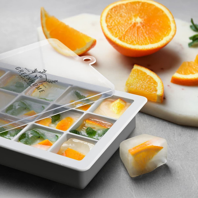 A Blizzard Ice Tray with Lid in white, featuring citrus and herb ice cubes; a sliced orange is nearby.