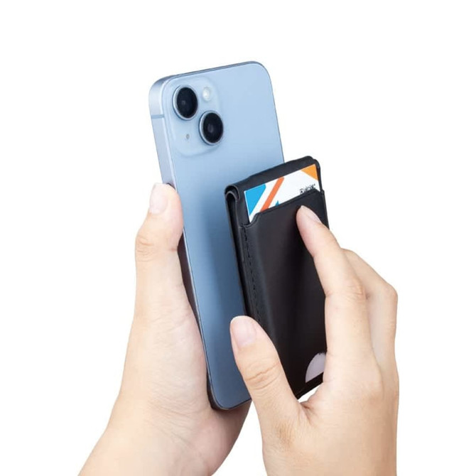 A black magnetic card wallet is being held against a smartphone, with credit cards inserted into the wallet.
