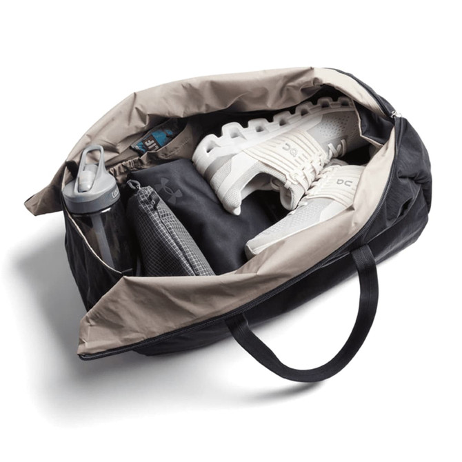 A black and beige duffel bag containing a water bottle, shoes, and a grey pouch. The bag has a logo.