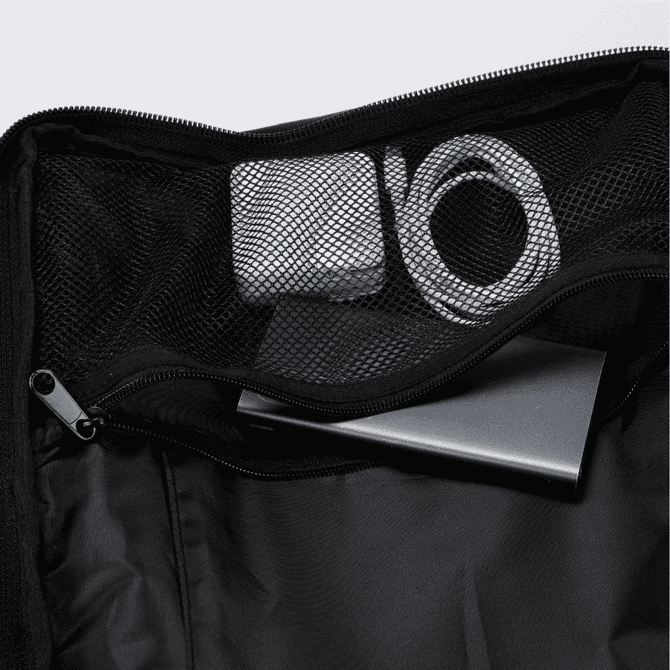 A black Eiger backpack interior featuring a metal device, tape, and a charging cable inside a mesh pocket.