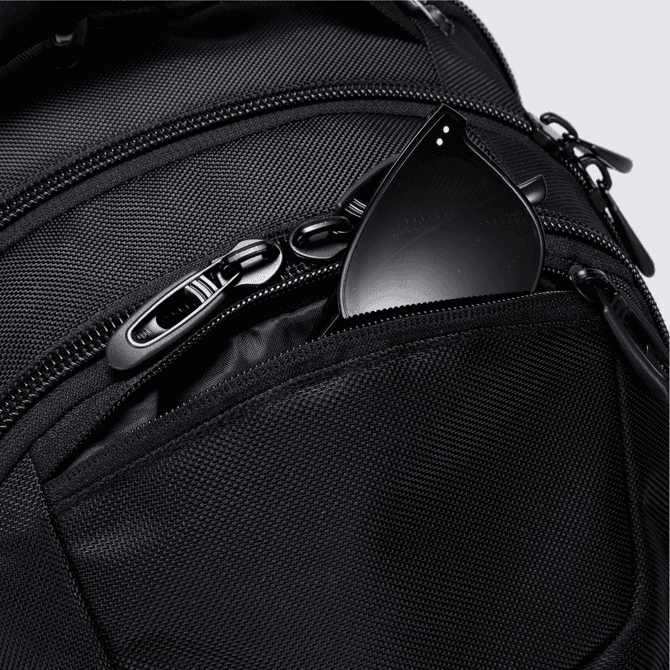 A black backpack with a textured finish and a small black item peeking from a front zippered pocket.
