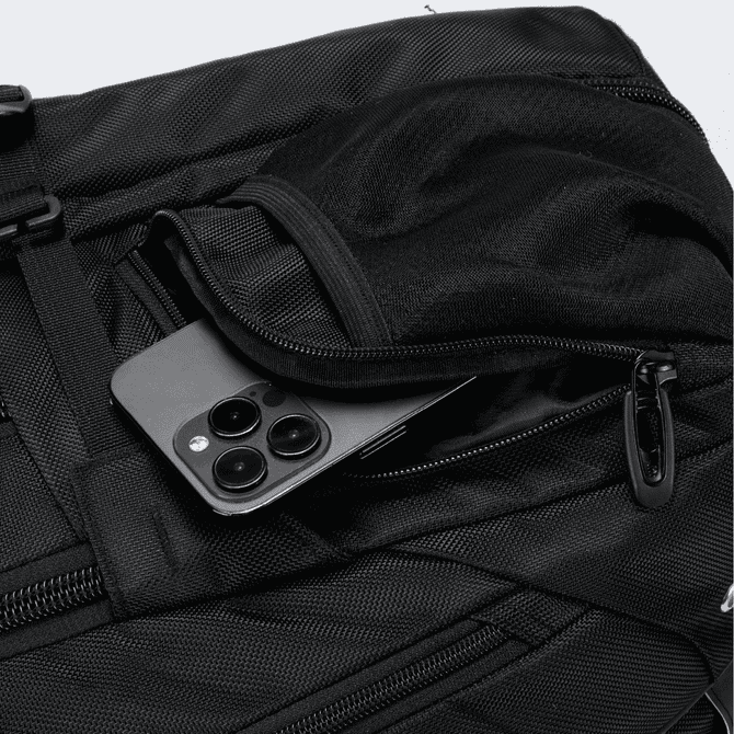 A black Eiger backpack with a smartphone tucked in a zippered pocket. The bag has a textured surface and features a logo.
