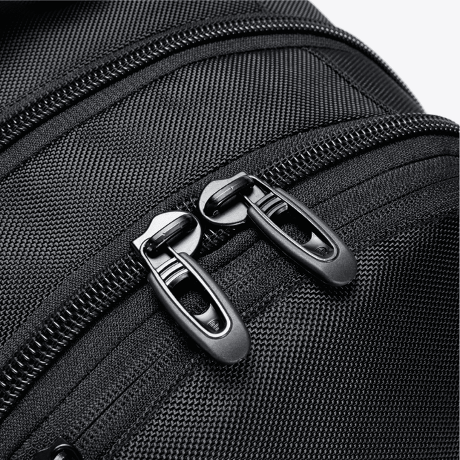 A close-up of a black backpack zipper, featuring dual zipper pulls and textured fabric.