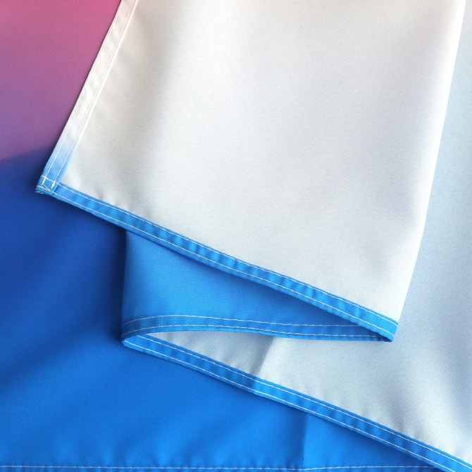 A large table runner featuring a gradient design with shades of blue and white. It has a stitched edge and branding.