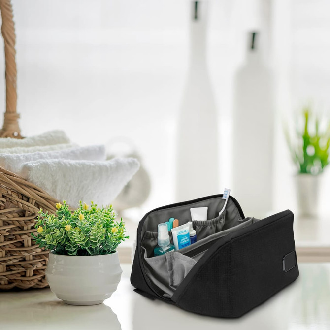 A black toiletry bag with various grooming products inside, set on a table near a plant and a woven basket.