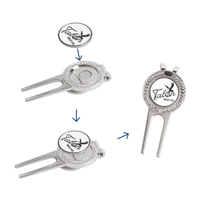 A silver golfers divot tool with a detachable ball marker, featuring a logo and intricate detailing.