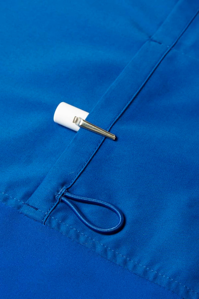 A close-up of a blue scrub top featuring a white toggle and a small metal clip.