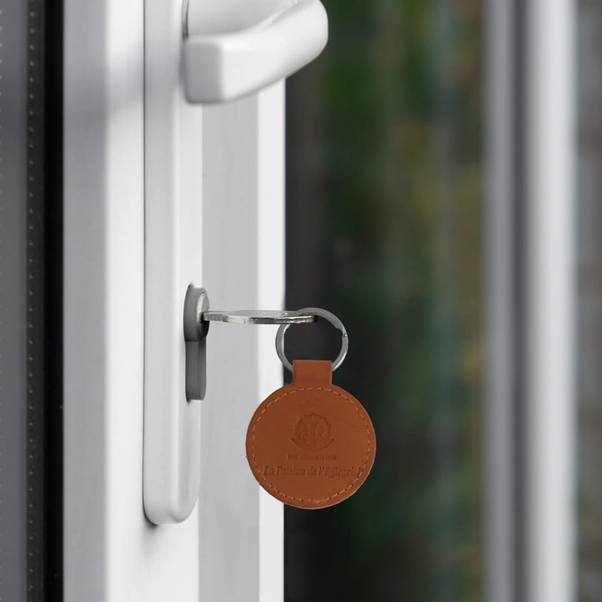 A round brown PU leather keyring attached to a silver key in a door lock.